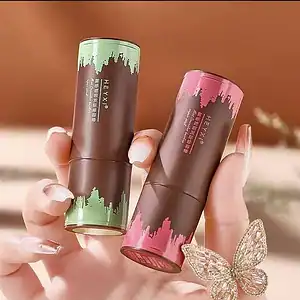 Two Hexy lip balm tubes in green and pink with cityscape design, held by a hand.